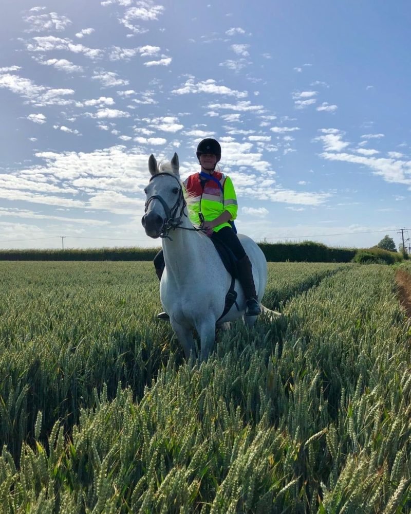 Beth riding a grey horse through a wheat field